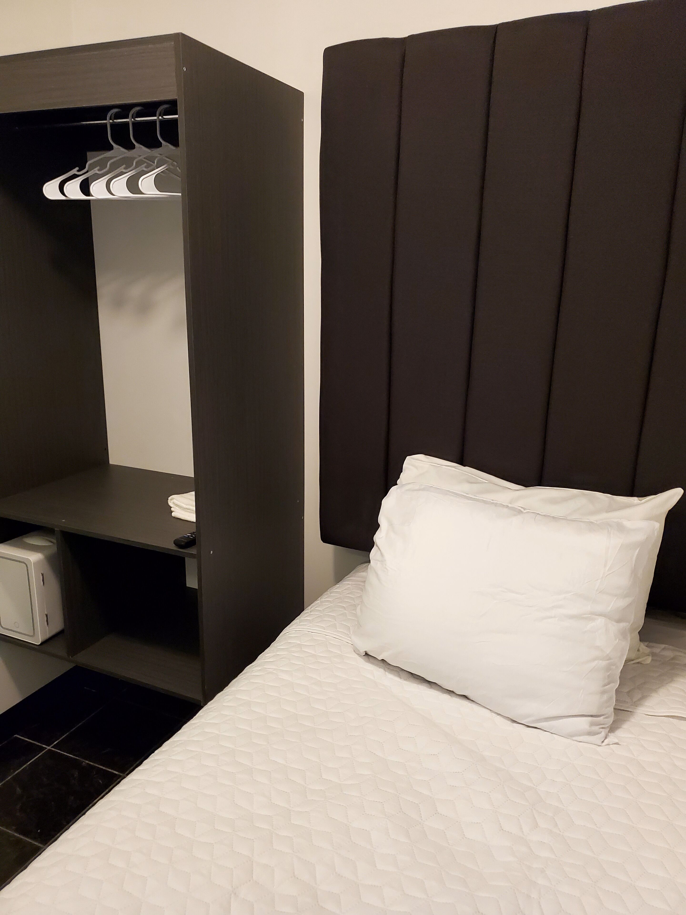 Una habitación de hotel con una cama, un armario y un pequeño escritorio con un mando a distancia.