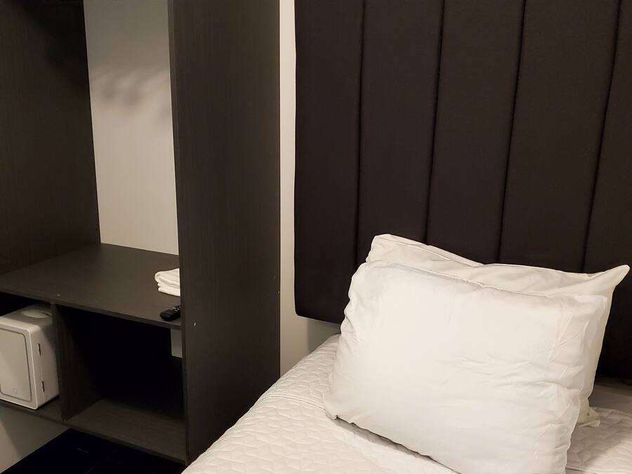 Una habitación de hotel con una cama, un armario y un pequeño escritorio con un mando a distancia.
