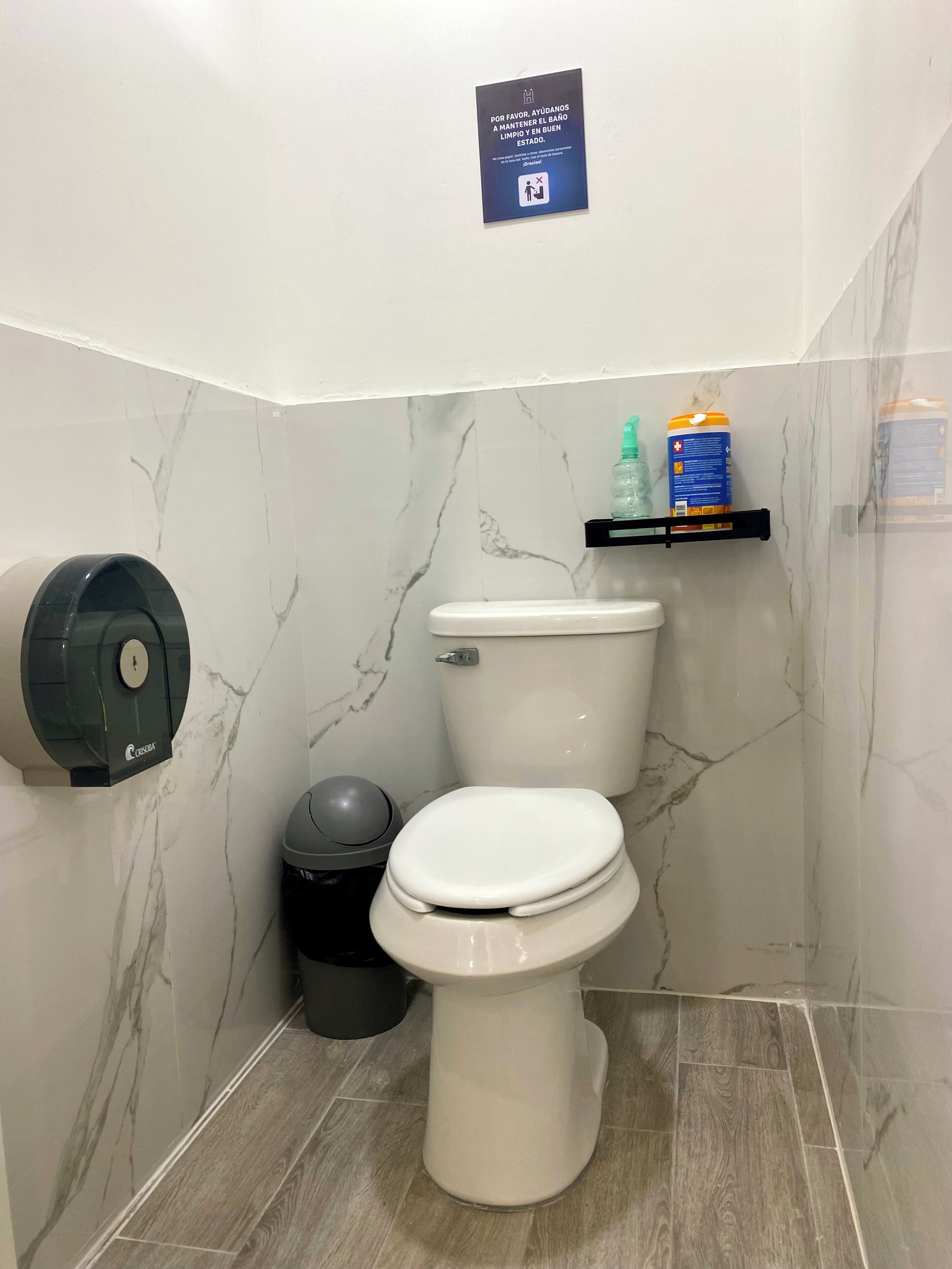 A bathroom with a toilet, a hand dryer, a trash bin, and a shelf with toiletries.