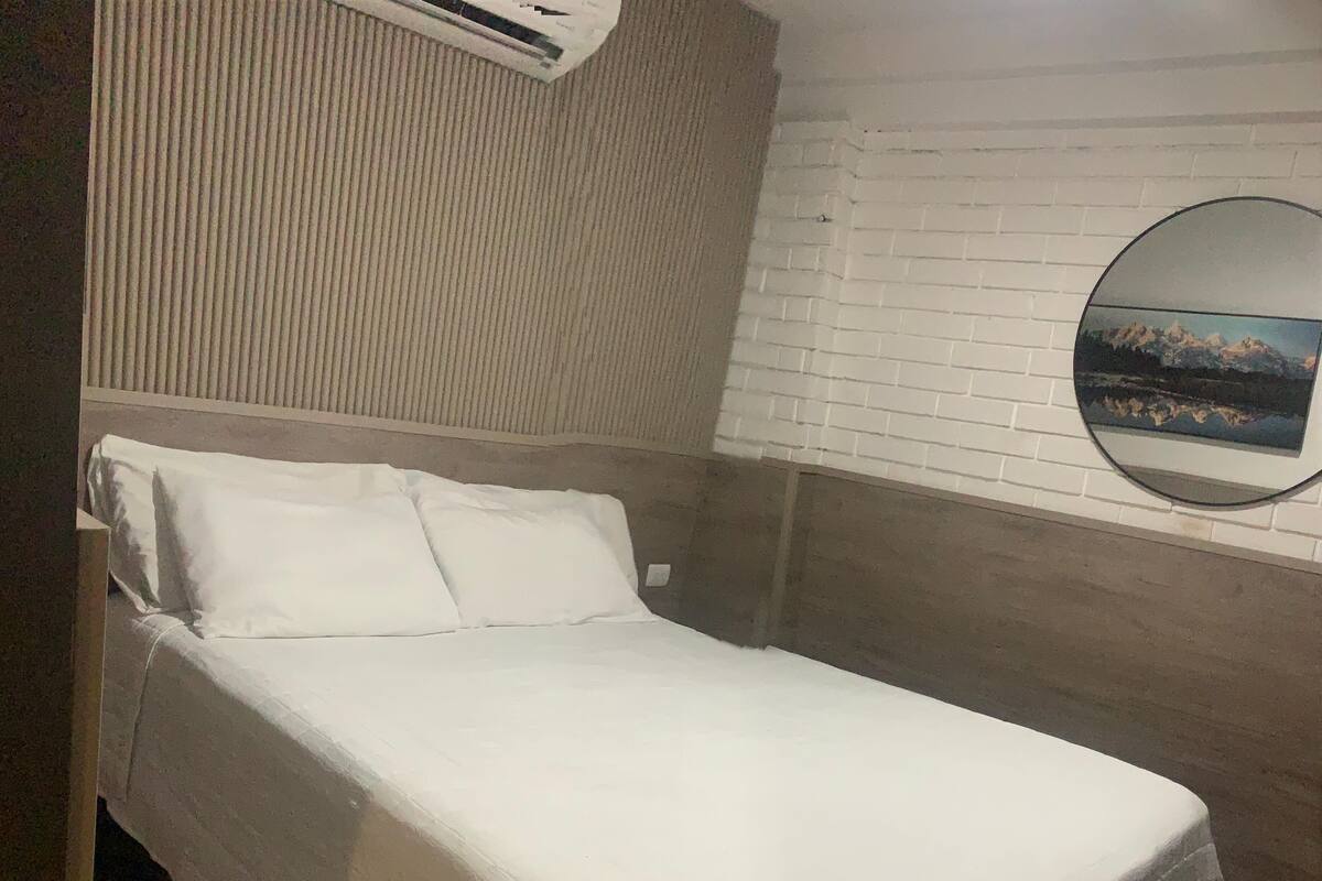 A single bed with a white bedspread in a room with a white brick wall and a round mirror.