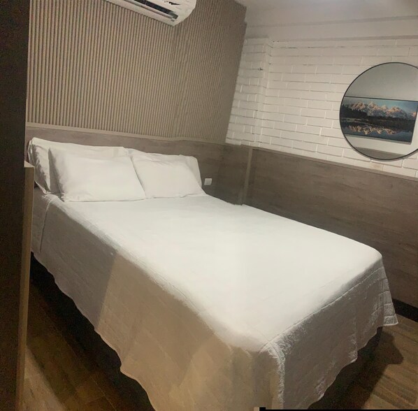 A single bed with a white bedspread in a room with a white brick wall and a round mirror. - Barrio Inn Padre Mier Hostal & Suites (Monterrey)