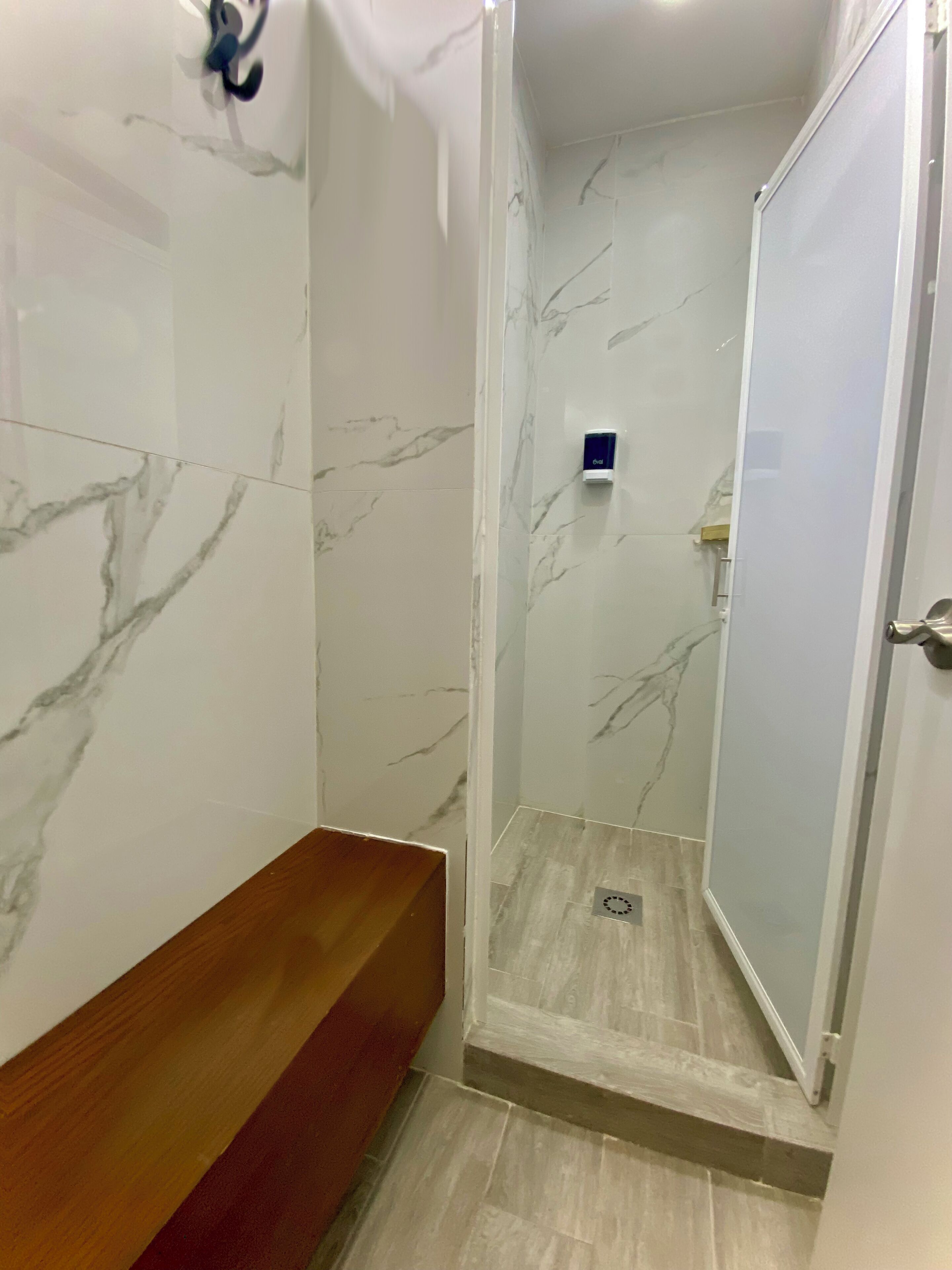 A bathroom with a shower enclosure, a wooden bench, and a marble wall.