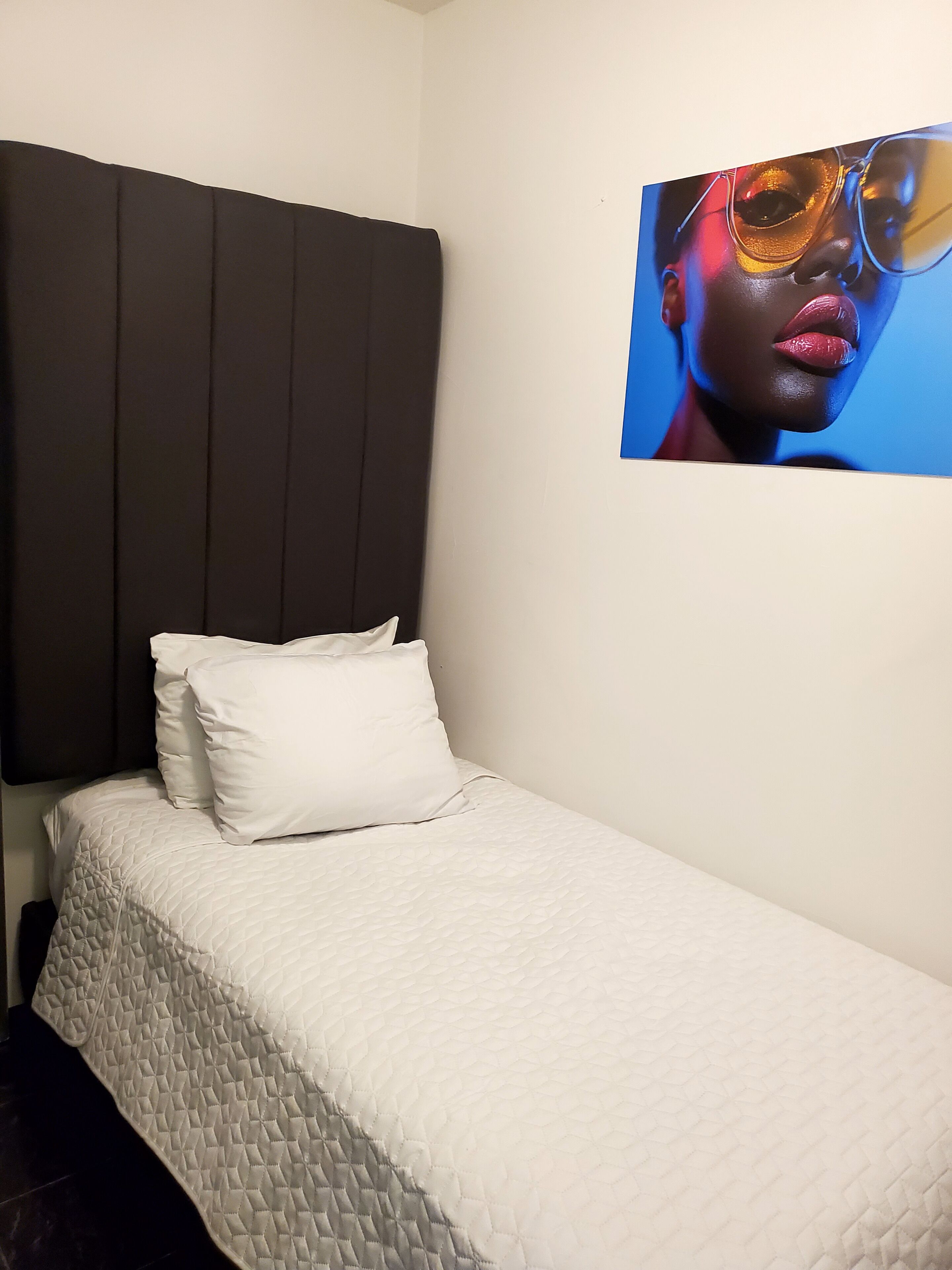 A single bed with a quilted white bedspread, a dark headboard, and a white pillow.