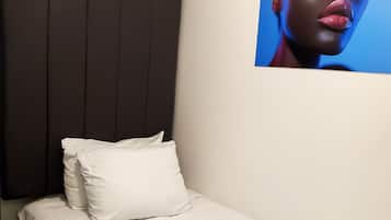 Een eenpersoonsbed met een gebogen wit sprei, een donker hoofdbord en een witte kussen.