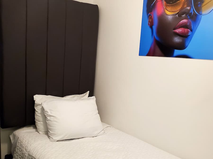 Een eenpersoonsbed met een gebogen wit sprei, een donker hoofdbord en een witte kussen.