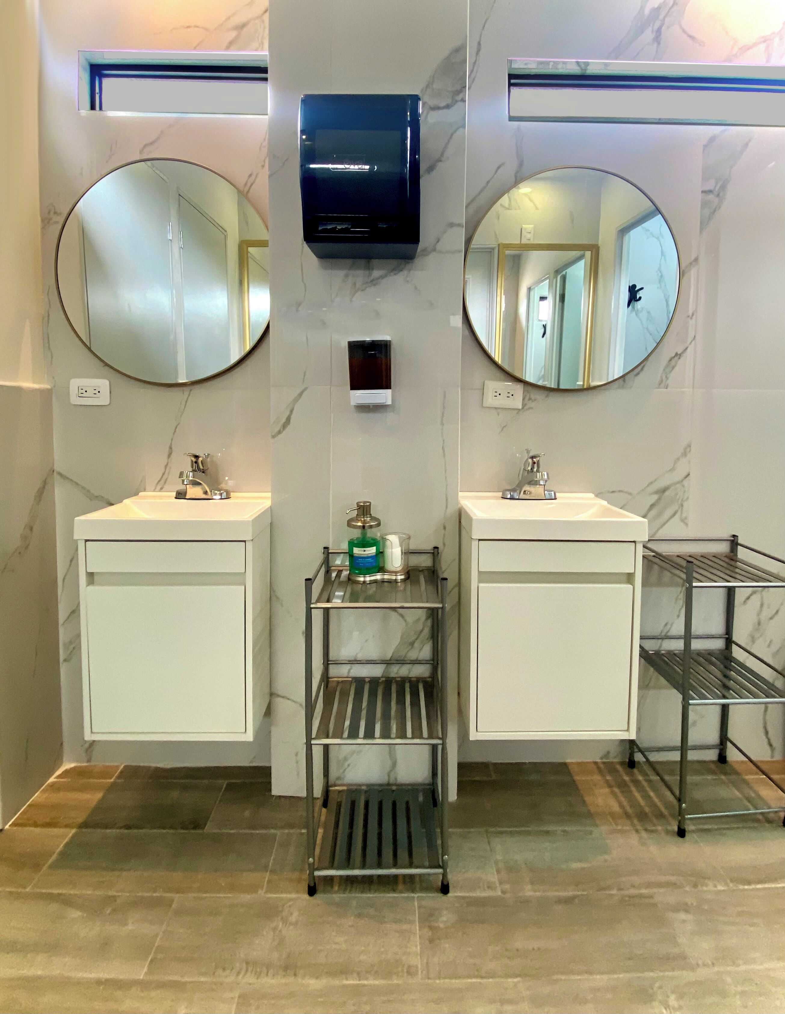 A bathroom with two sinks, two mirrors, a television, and a metal rack with toiletries.