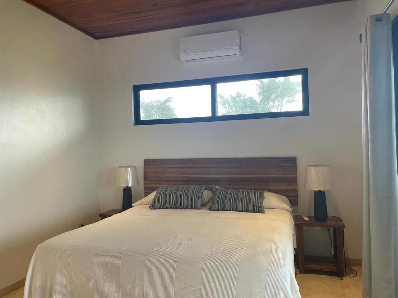 Une chambre à coucher avec un grand lit, deux tables de chevet avec des lampes, une fenêtre et un appareil de climatisation.