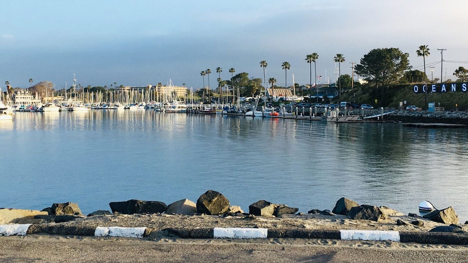 A marina with boats docked, a rocky shoreline, and a sign that reads "OCEANS."