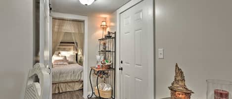 A hallway with a bed, a wall-mounted shelf with various items, and a small table with decorative objects.