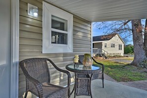 Eine überdachte Veranda mit Korbstühlen und einem Glastisch, ein Fenster mit Leuchte und ein Blick auf ein Haus im Hintergrund.