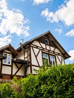 Ein traditionelles Fachwerkhäuschen mit erkennbarem Schornstein, einem Fenster und blauem Himmel.