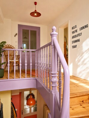 Eine Treppe mit einer violetten Geländer führt zu einer Zwischenebene mit einer Tür.