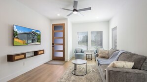 Una sala de estar moderna con una televisión de pantalla plana, ventilador de techo, sofá, mesa de centro y una puerta que da al exterior.
