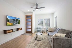 Ein modernes Wohnzimmer mit Fernseher, Deckenventilator, Sofa, Couchtisch und einer Tür, die nach draußen führt.
