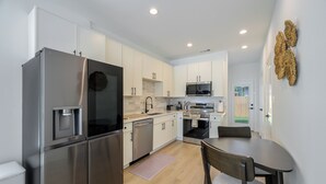 Una cocina moderna con electrodomésticos de acero inoxidable, armarios blancos y un comedor con mesa y sillas.