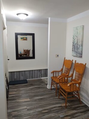 Una habitación con piso de madera, un espejo con un cuadro y dos sillas de madera.