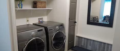 A laundry room with two front-loading washers and dryers, a shelf with a basket, a mirror, and a wooden floor.