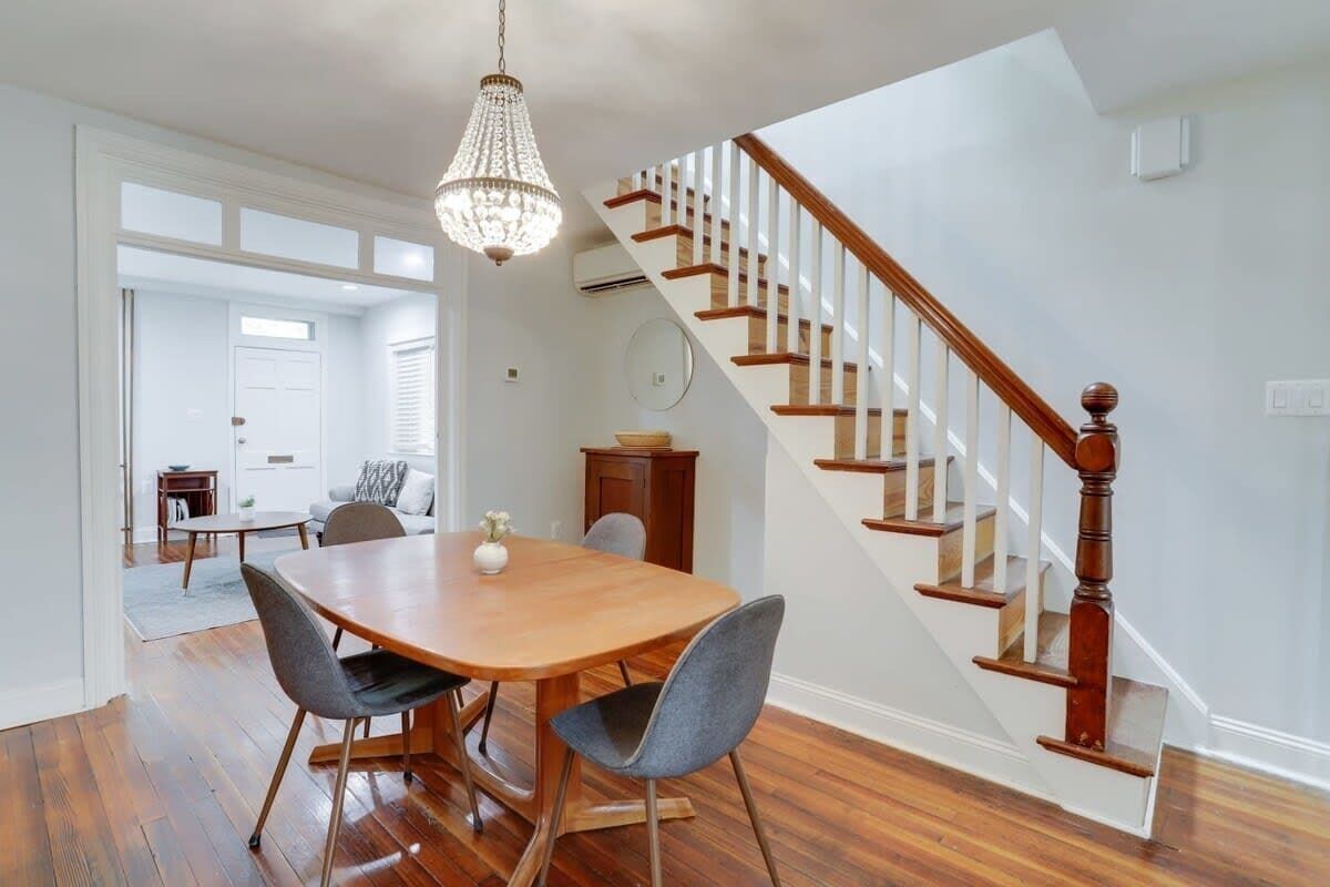 A dining area with a wooden table and chairs, a chandelier, and a staircase with wooden railings.