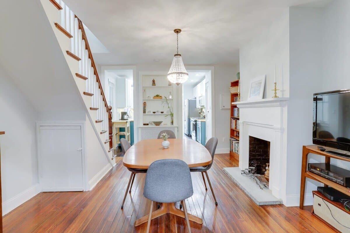 A dining area with a wooden table, chairs, a chandelier, a fireplace, and a TV stand.