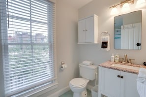 A bathroom with a toilet, sink, mirror, cabinet, and window with blinds. - Sojourn 2BD on Historic Capitol Hill (Washington DC)