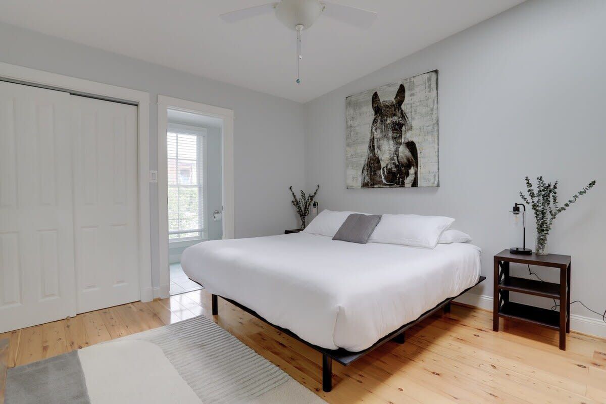 A bedroom with a bed, a ceiling fan, a door, a window, and a wall-mounted artwork.