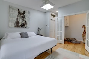 A bedroom with a bed, a ceiling fan, a door leading to another room, and a giraffe statue. - Sojourn 2BD on Historic Capitol Hill (Washington DC)