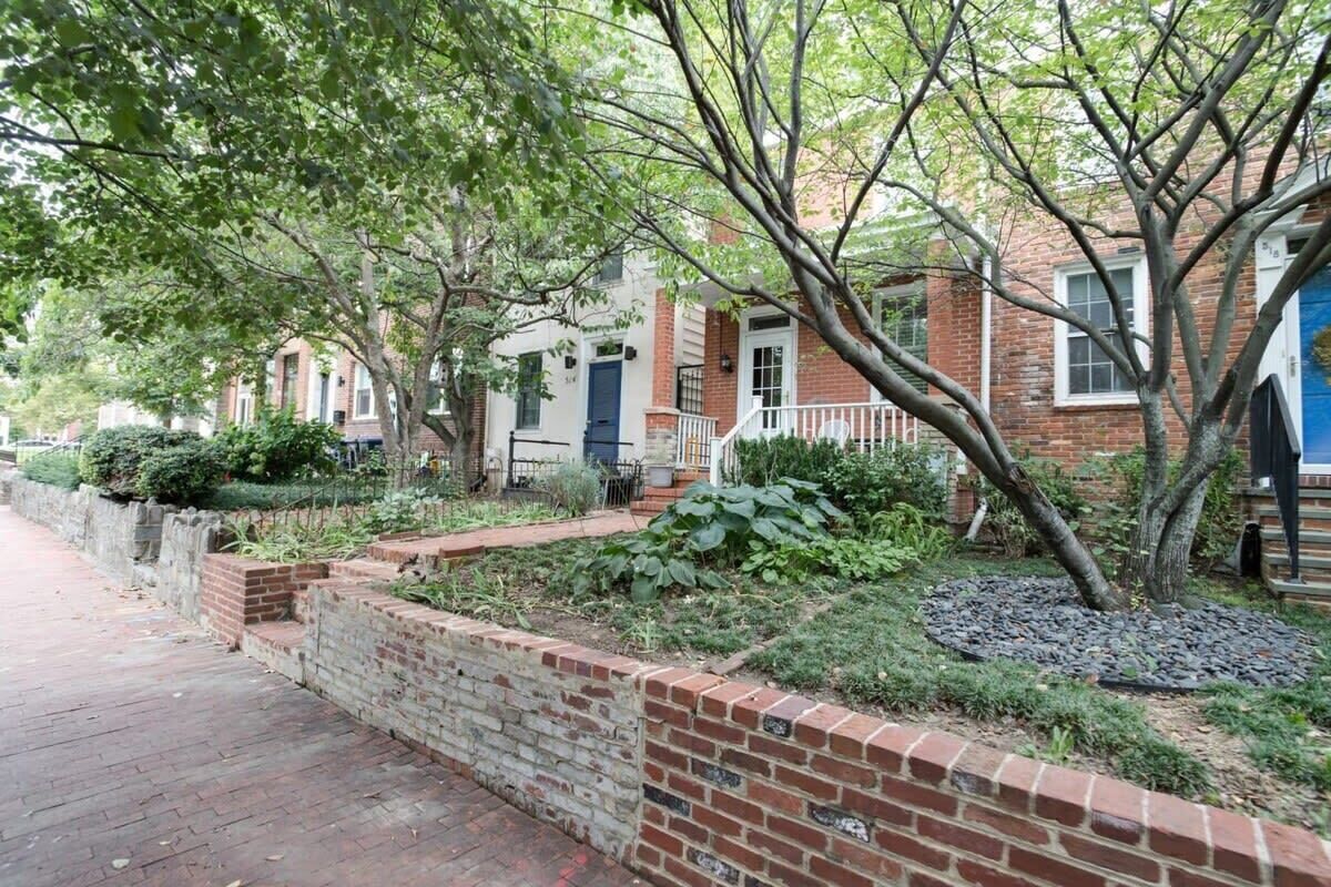 A row of brick townhouses with a brick pathway and greenery.