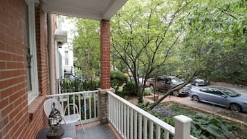 A covered porch with a brick wall, white railing, and a table with chairs.