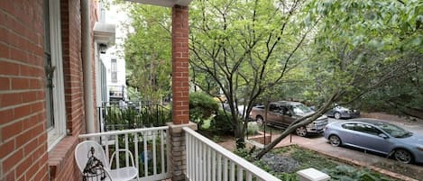 A covered porch with a brick wall, white railing, and a table with chairs.
