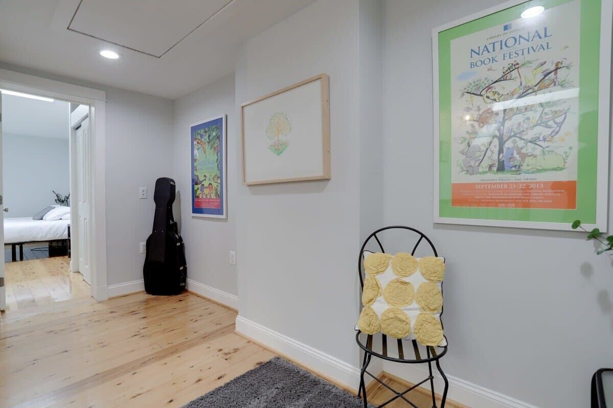 A room with a bed, a guitar, a chair with a cushion, and a poster on the wall.