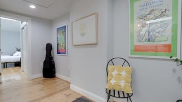 A room with a bed, a guitar, a chair with a cushion, and a poster on the wall.