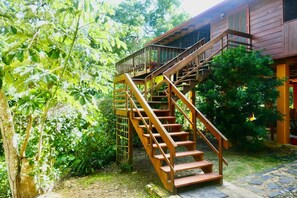 Una escalera de madera que conduce a un edificio de madera con balcón, rodeado de exuberante follaje.