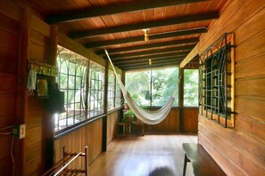 A wooden interior with a hammock, large windows, and a view of greenery.