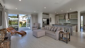 A modern living room with a sofa, a chair, a small table, and a kitchen area with a fridge and stove. - Waterfront Base with Private Pontoon and Kayaks (One Tree Point)
