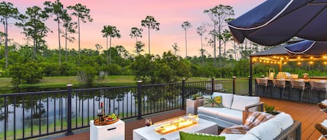 A deck with outdoor furniture, a fire feature, and a view of a lake and trees.