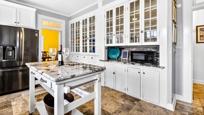 A modern kitchen with white cabinetry, a granite countertop, a stainless steel refrigerator, and a microwave. - Historic Midtown Brick Home with Fire Pit (Columbus)