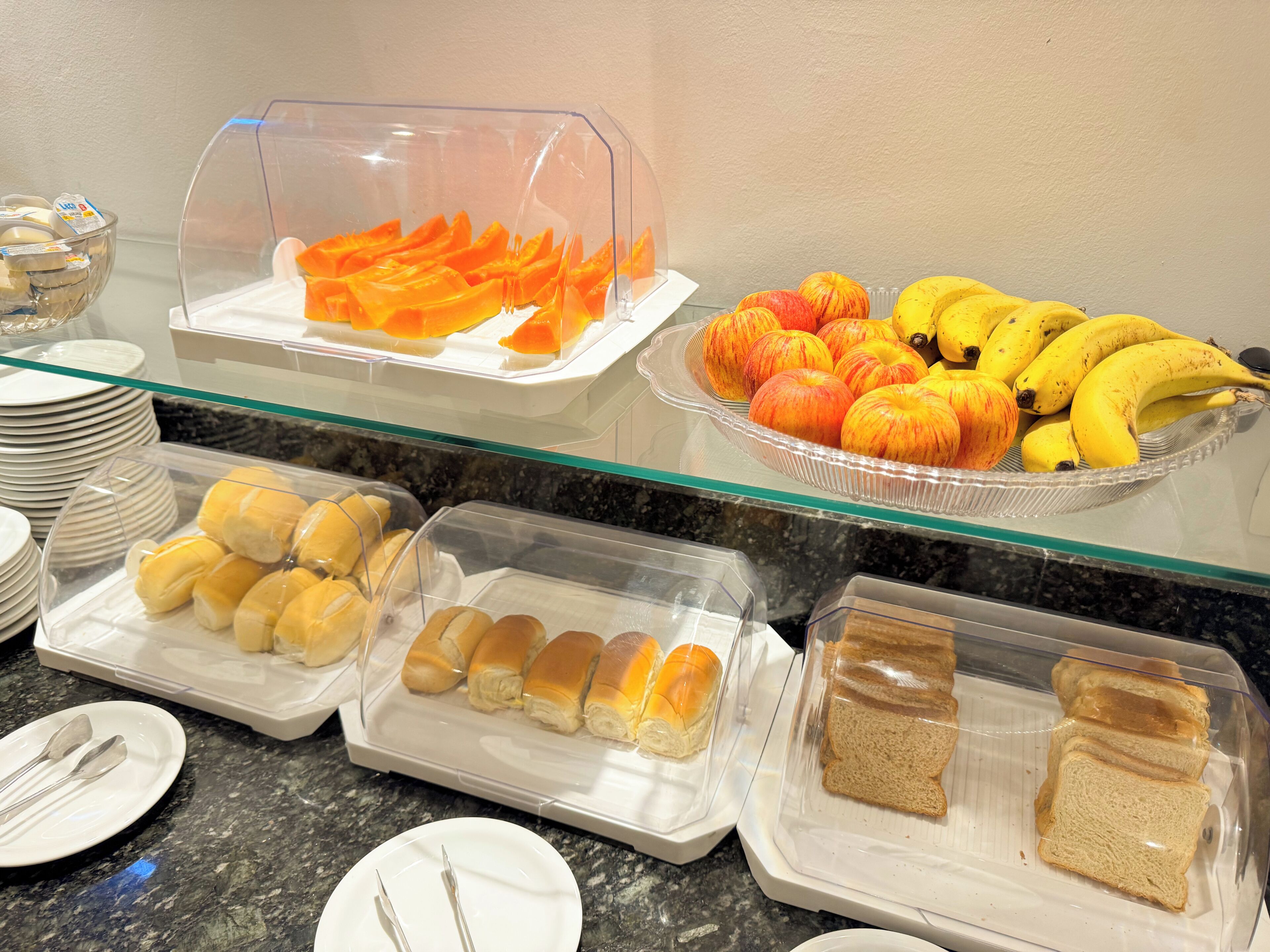 A buffet with various food items including bread, rolls, and fruits like apples and bananas.