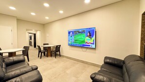 A conference room with a television displaying a sports event, a table with chairs, and leather sofas.