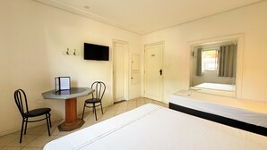 A hotel room with a bed, a desk with a chair, a television, and a window with curtains.
