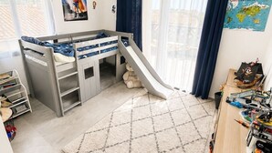 Une chambre d’enfant avec des lits superposés, un toboggan, un bureau avec des jouets et une carte du monde accrochée au mur.