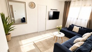 Un salon moderne avec un canapé, un téléviseur à écran plat, un miroir et une plante en pot.
