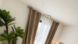 Une chambre à coucher avec un lit, des rideaux, une plante en pot et une table de chevet.