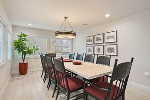 A dining room with a large table, chairs, a potted plant, and framed pictures on the wall. - Weldons' Kyle Field Cottage (College Station)