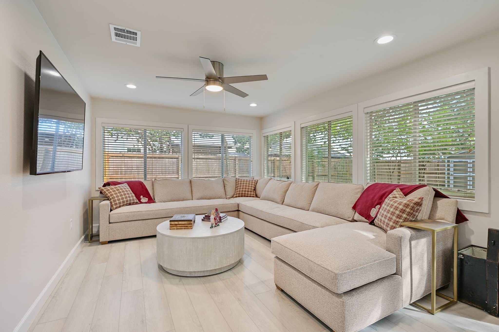 A modern living room with a sectional sofa, a round coffee table, and large windows with blinds.