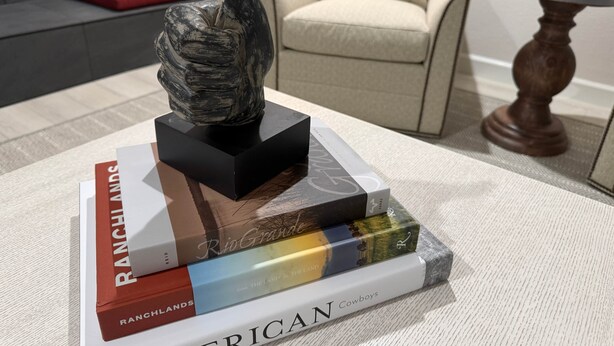 Una escultura sobre un pedestal negro, rodeada de libros titulados 'Ranchlands', 'Rio Grande' y 'American Cowboys'.