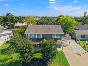 A residential house with a front yard, a covered porch, and a basketball court. - Weldons' Kyle Field Cottage (College Station)
