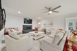 A modern living room with a flat-screen TV, a ceiling fan, and a fireplace. - Weldons' Kyle Field Cottage (College Station)
