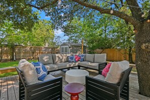 An outdoor seating area with a sectional sofa, two armchairs, and a round table. - Weldons' Kyle Field Cottage (College Station)