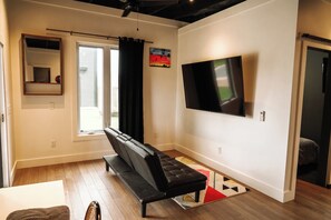A living room with a black sofa, a flat-screen TV, a window with curtains, a painting, and a ceiling fan. - Marion Cabin private pool, pickleball, park, walking paths, and put-put golf (Marion)