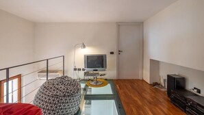 A modern living room with a glass coffee table, a patterned ottoman, a television, and a black entertainment unit. - Venezia Terrace (Florence)